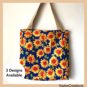 May include: A blue tote bag with a sunflower print. The bag has tan straps and the text "3 Designs Available" is visible on the left side of the bag.