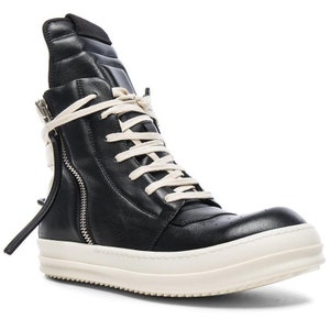 K&ouml;nnte beinhalten: Schwarze High-Top-Sneaker aus Leder mit wei&szlig;er Gummisohle und einem Rei&szlig;verschluss an der Seite. Die Schn&uuml;rsenkel sind wei&szlig; und in einer Schleife gebunden.