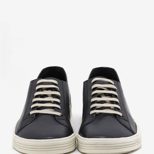 K&ouml;nnte beinhalten: Ein Paar schwarze Leder-Sneaker mit wei&szlig;en Schn&uuml;rsenkeln und einer wei&szlig;en Gummisohle.