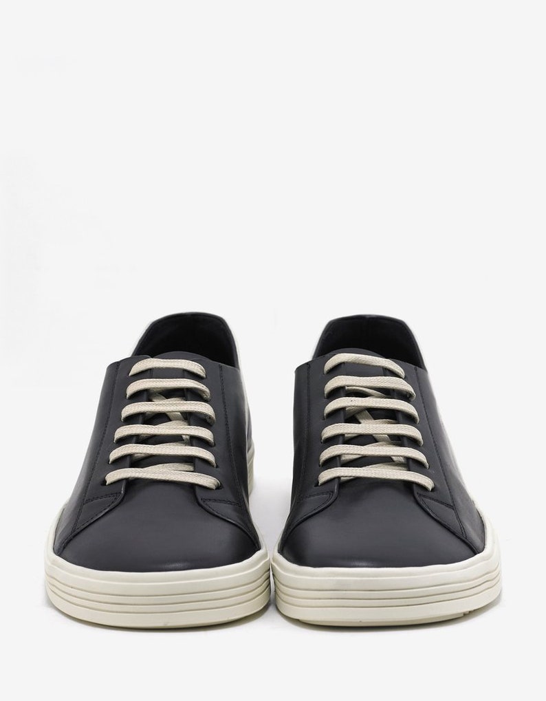 K&ouml;nnte beinhalten: Ein Paar schwarze Leder-Sneaker mit wei&szlig;en Schn&uuml;rsenkeln und einer wei&szlig;en Gummisohle.
