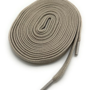 K&ouml;nnte beinhalten: Ein Paar beige Schn&uuml;rsenkel, aufgerollt und auf einem wei&szlig;en Hintergrund ausgelegt.