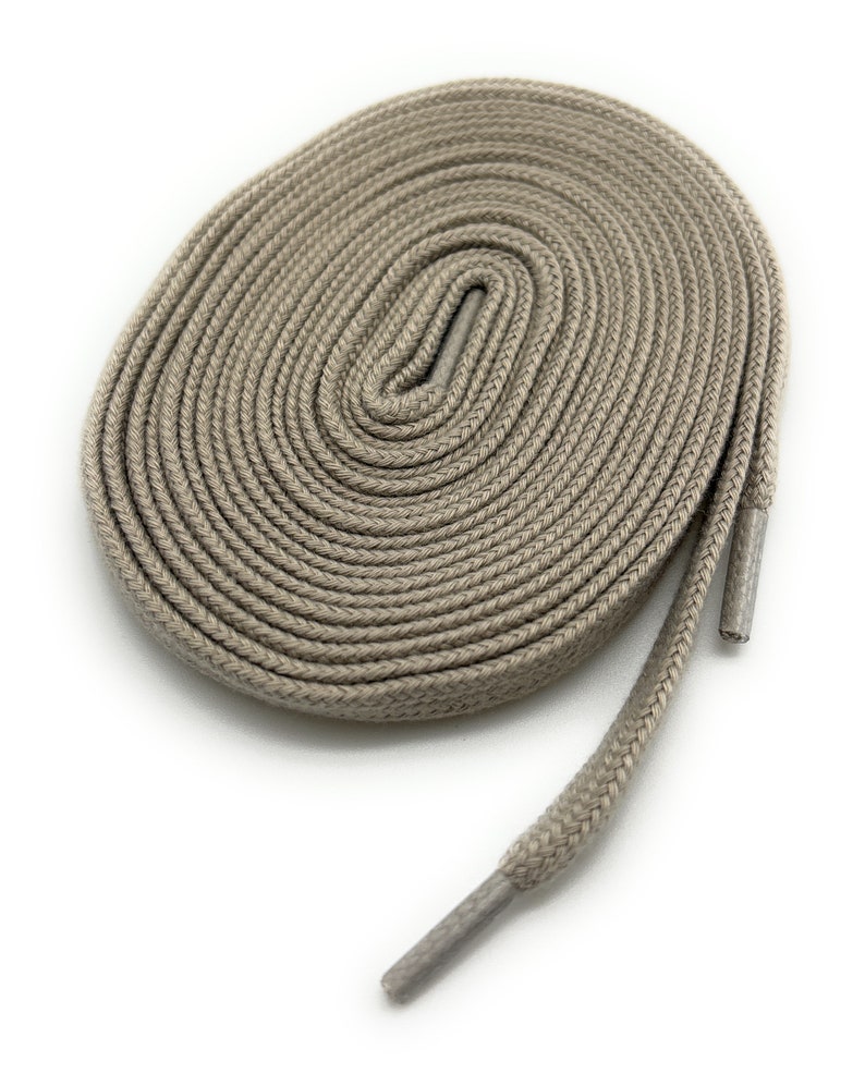 K&ouml;nnte beinhalten: Ein Paar beige Schn&uuml;rsenkel, aufgerollt und auf einem wei&szlig;en Hintergrund ausgelegt.