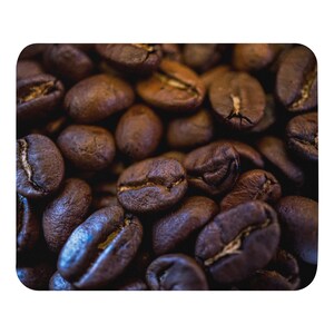 May include: A dense collection of roasted coffee beans, each featuring a deep brown color and a distinct central fissure. The beans exhibit a matte, textured surface with varying shades of dark brown, showing a consistent oval shape throughout.