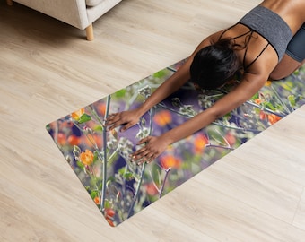 May include: A rectangular yoga mat featuring a vibrant photographic print of orange wildflowers and green stems against a blurred purple and green background. The mat has rounded corners and is positioned flat on a light-colored wooden floor surface.