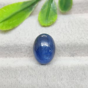 May include: A polished, oval-shaped blue gemstone with a smooth, reflective surface. The stone displays a deep, saturated blue color with subtle variations in tone and internal clarity, characteristic of a cabochon-cut precious or semi-precious stone.