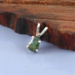 May include: A pear-shaped green gemstone pendant with a silver bail. The pendant is set in a silver setting with four prongs.