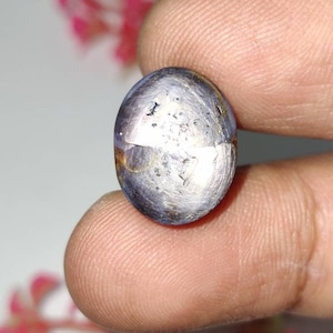 Pode incluir: Uma gema ovalada prateada com um padrão em forma de estrela no centro. A gema está engastada em um anel de prata.