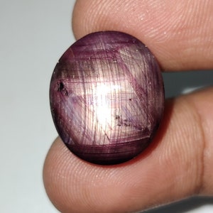 May include: A round, purple gemstone with a star-like pattern. The gemstone is set in a silver ring.