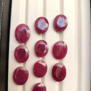 Puede incluir: Doce piedras preciosas sueltas, talladas, de forma ovalada, de color rojo rubí, expuestas en una caja blanca forrada.
