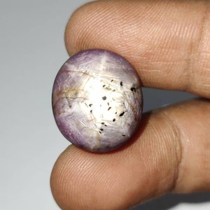 May include: A purple and silver star ruby gemstone with a cabochon cut. The gemstone has a star-like pattern and is set in a silver ring.