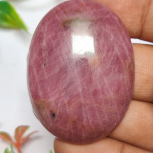 May include: A pink oval cabochon gemstone with a striated pattern. The gemstone is smooth and polished.
