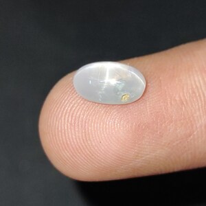 Puede incluir: Una piedra preciosa ovalada blanca con un patr&oacute;n en forma de estrella y una peque&ntilde;a inclusi&oacute;n dorada.