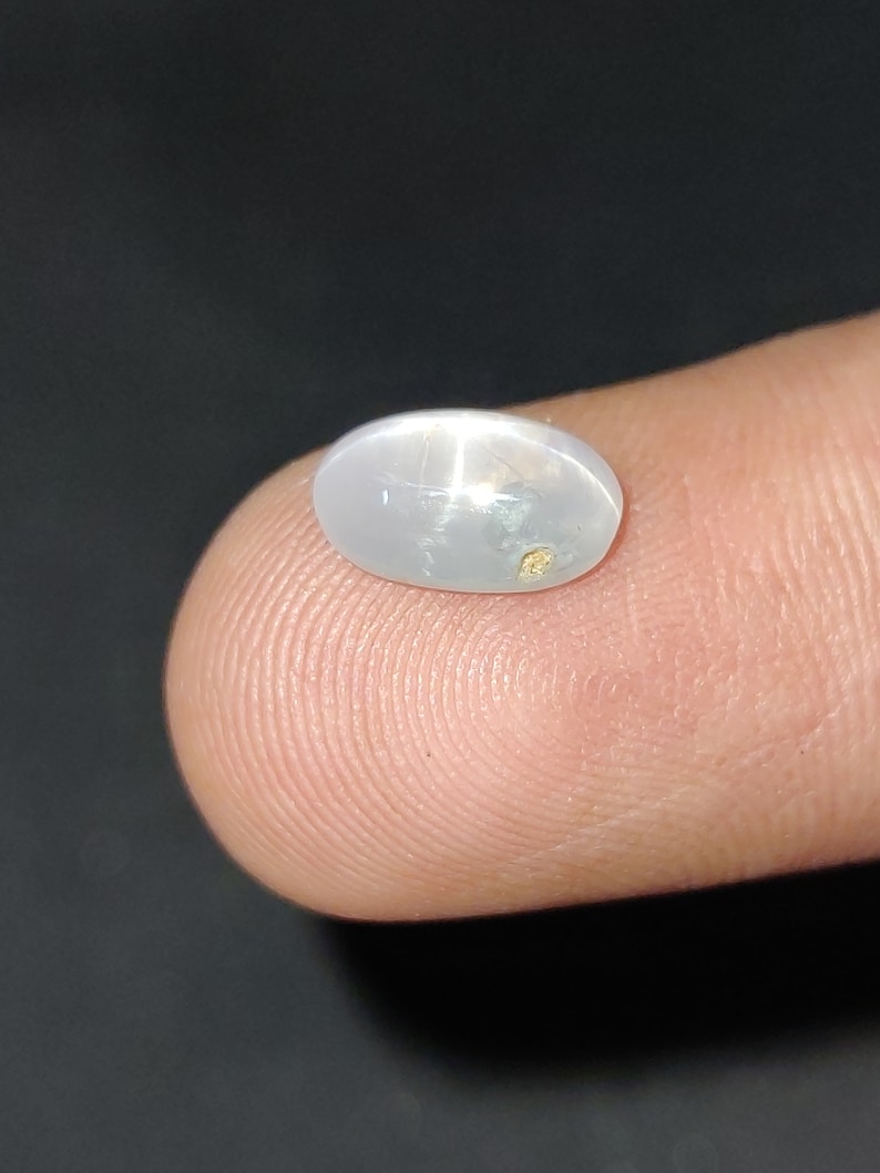 Puede incluir: Una piedra preciosa ovalada blanca con un patr&oacute;n en forma de estrella y una peque&ntilde;a inclusi&oacute;n dorada.