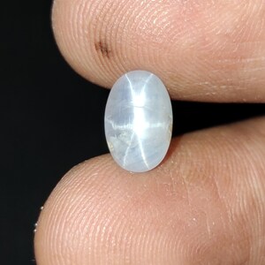 Puede incluir: Una piedra preciosa de zafiro estrella ovalada de color blanco con un patr&oacute;n en forma de estrella en el centro.