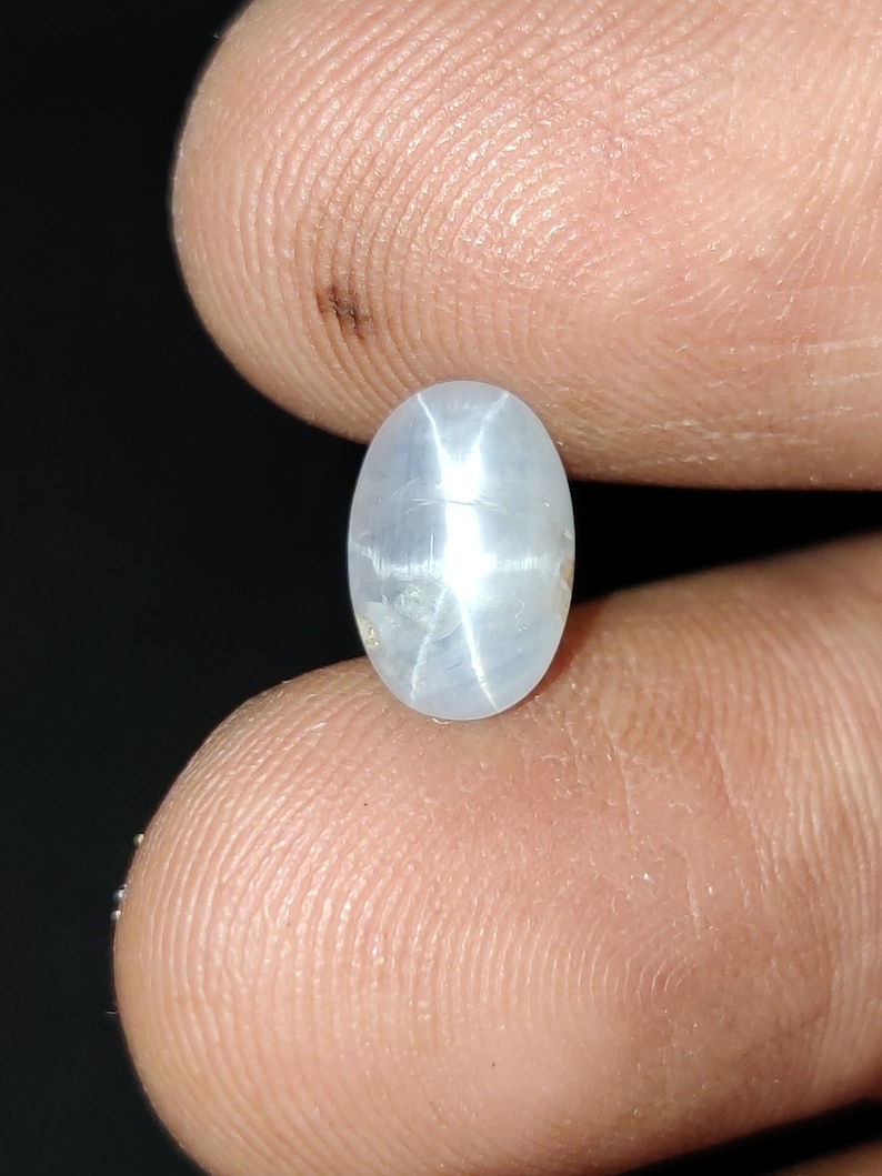 Puede incluir: Una piedra preciosa de zafiro estrella ovalada de color blanco con un patr&oacute;n en forma de estrella en el centro.