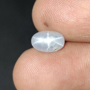 Puede incluir: Una piedra preciosa de zafiro estrellado ovalada de color azul claro con un patr&oacute;n en forma de estrella en el centro.