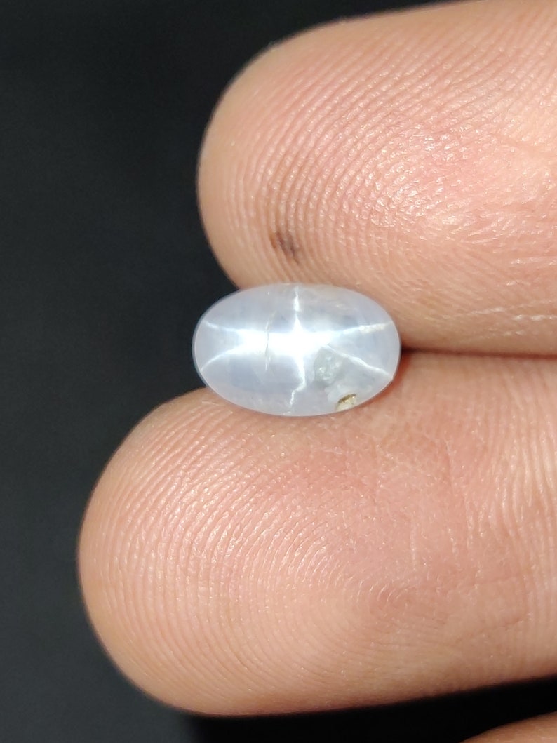 Puede incluir: Una piedra preciosa de zafiro estrellado ovalada de color azul claro con un patr&oacute;n en forma de estrella en el centro.