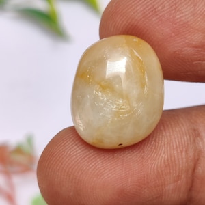May include: A smooth, oval-shaped, light yellow gemstone with a white center and brown swirls.