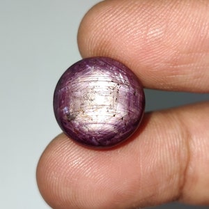 May include: A round, cabochon-cut, purple ruby gemstone with a star-like pattern in the centre. The stone is set in a silver ring.