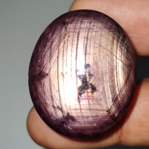 May include: A large, oval-shaped, purple gemstone with a silvery sheen and a striated pattern. The gemstone is set in a cabochon cut.