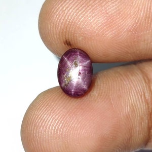 May include: A deep red star ruby gemstone with a six-pointed star in the center. The ruby is oval shaped and has a polished finish.