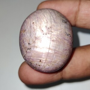 Könnte beinhalten: Ein runder, cabochon geschliffener, violetter Edelstein mit silbernem Schimmer und einem gestreiften Muster. Der Edelstein ist in einem Silberring gefasst.