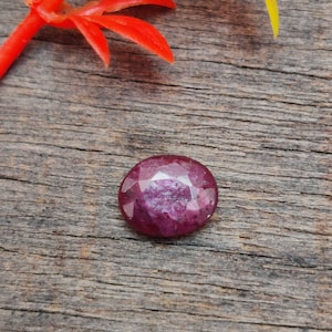 Könnte beinhalten: Ein tiefrosa Edelstein mit facettiertem Schliff, vor einem rustikalen Holz Hintergrund.