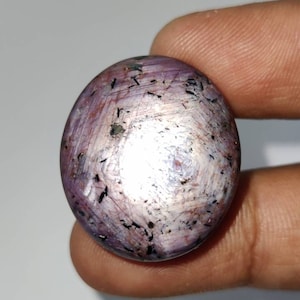 Op de afbeelding: Een ronde, paarse edelsteen met een stervormig patroon en zwarte insluitsels.