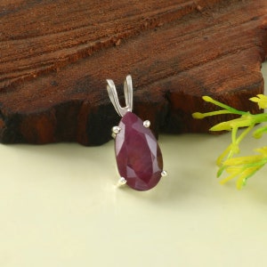 May include: A pear-shaped ruby pendant set in sterling silver. The ruby is a deep red color and has a faceted cut. The pendant is on a white background.