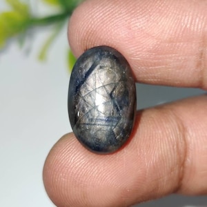 May include: A dark blue oval-shaped gemstone with a star-like pattern inside. The gemstone is set in a silver ring.
