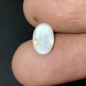 Puede incluir: Una piedra preciosa ovalada blanca con motas doradas, engastada en un cabuj&oacute;n ovalado transparente.