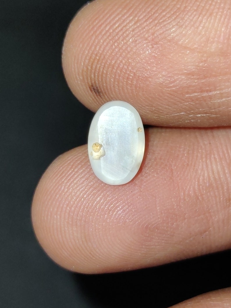 Puede incluir: Una piedra preciosa ovalada blanca con motas doradas, engastada en un cabuj&oacute;n ovalado transparente.