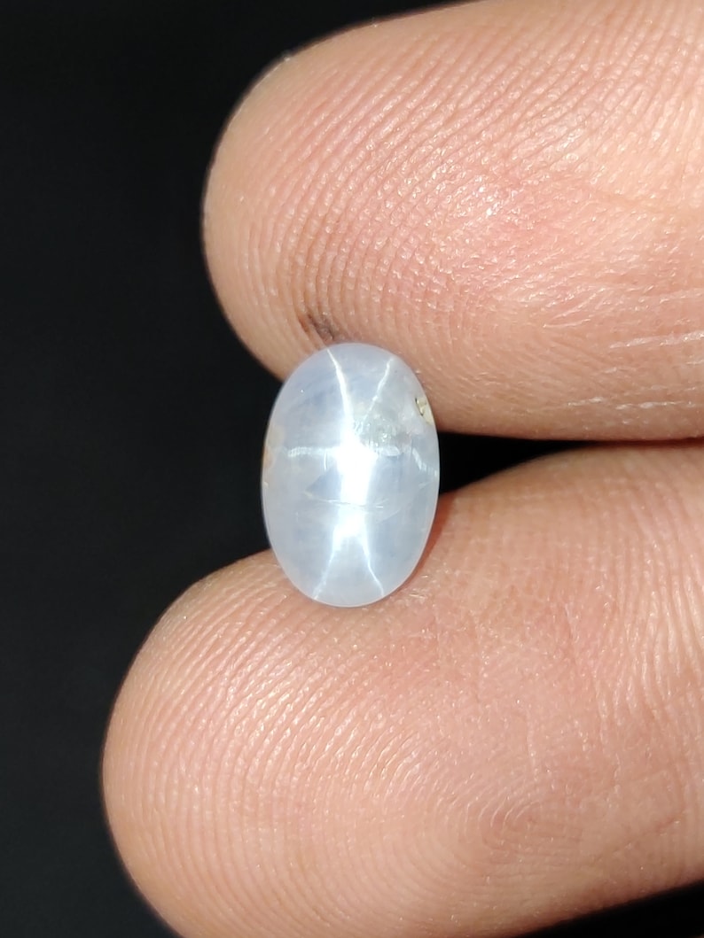 Puede incluir: Una piedra preciosa de zafiro estrella ovalada blanca con un patr&oacute;n en forma de estrella en el centro.