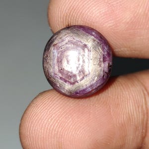 May include: A round, purple gemstone with a star-shaped pattern in the center. The gemstone is set in a silver ring.