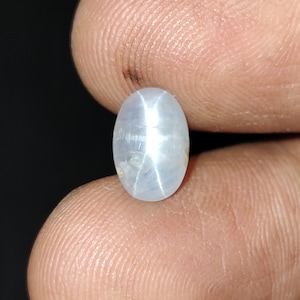 Puede incluir: Una piedra preciosa de zafiro estrella ovalada de color blanco con un patr&oacute;n en forma de estrella en el centro.