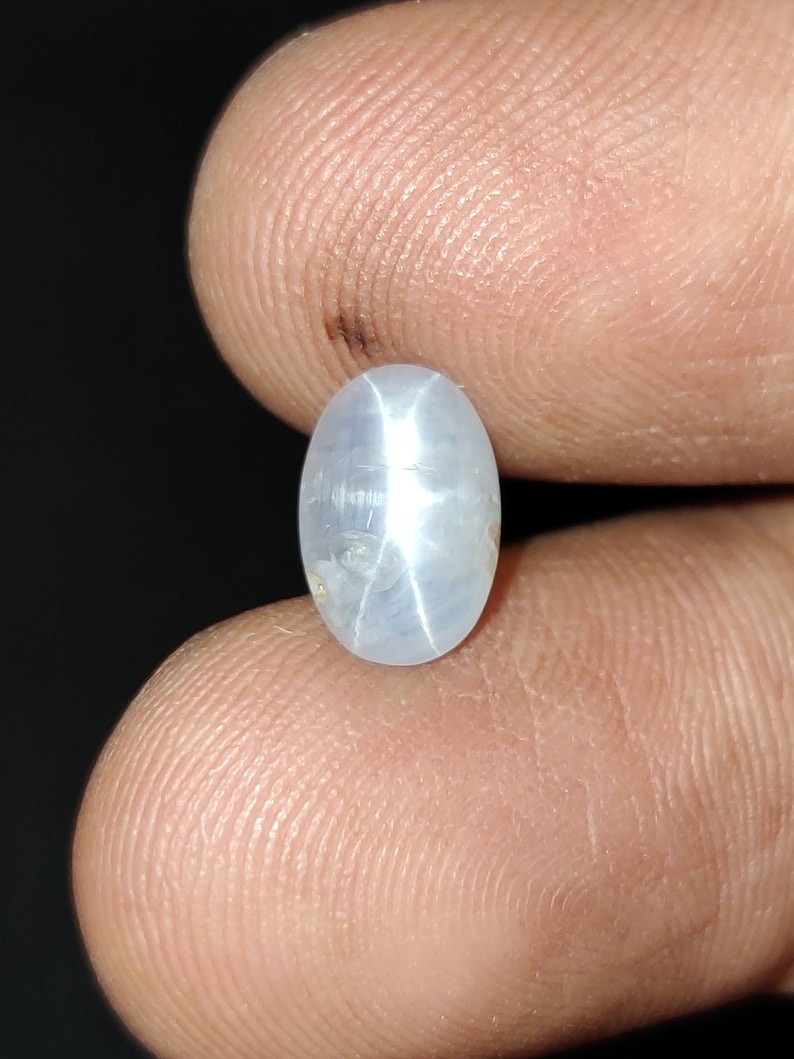 Puede incluir: Una piedra preciosa de zafiro estrella ovalada de color blanco con un patr&oacute;n en forma de estrella en el centro.