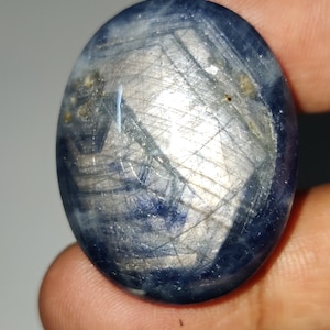 Könnte beinhalten: Ein blauer ovaler Edelstein mit silbernem Schimmer und einem sternförmigen Muster.
