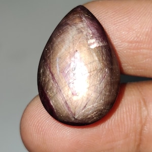 May include: A teardrop-shaped gemstone with a star-like pattern and a mix of purple, pink, and gold hues.