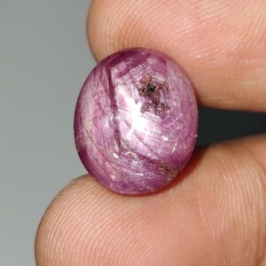 May include: A pink ruby gemstone with a star-like pattern, cabochon cut and polished.