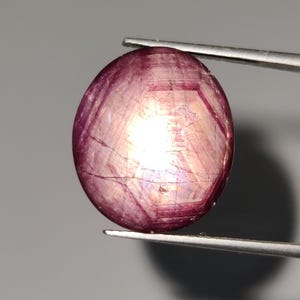 Puede incluir: Una piedra preciosa ovalada de color rosa con un patrón en forma de estrella y un centro blanco.