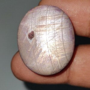 May include: A round, iridescent gemstone with a white and purple color. The gemstone has a smooth, polished surface with visible striations.