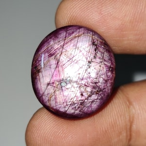 May include: A round, cabochon-cut, pink ruby gemstone with a star-like pattern of inclusions. The stone has a deep pink colour and is set in a silver ring.