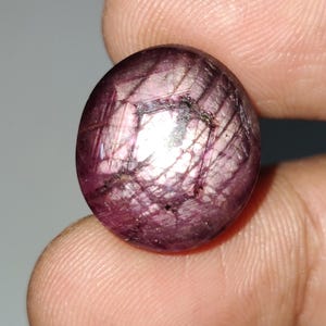 May include: A round, pink ruby gemstone with a star-like pattern inside. The gemstone is set in a silver ring.