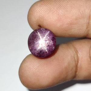Può includere: Una pietra preziosa di rubino stella rotonda, di colore viola, con una stella a sei punte al centro.