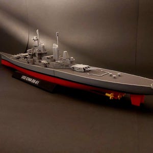 以下が含まれることがあります： USSアイオワBB-61戦艦の模型。 灰色の船は赤い喫水線があり、黒い台座に取り付けられています。 モデルは、詳細な砲塔、マスト、その他の船のコンポーネントを備えています。 テキスト「USS Iowa BB-61」が表示されています。