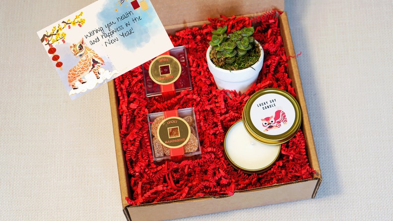 A gift box filled with red paper and four gifts with a card next to it