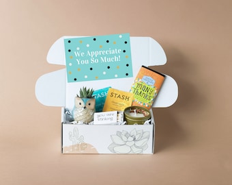 May include: A white gift box with a cactus design, filled with a variety of gifts, including a small succulent in a ceramic owl planter, a candle, matches, tea bags, and a chocolate bar. The box also includes a card that reads "We Appreciate You So Much!"