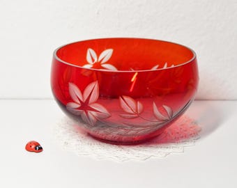 Könnte beinhalten: Eine leuchtend rote Glasschale mit geätzten Blumenmustern. Die Schale hat weiße Blumen- und Blattmuster und steht auf einer weißen Spitzendeckchen. Eine kleine Marienkäferfigur befindet sich neben der Schale.