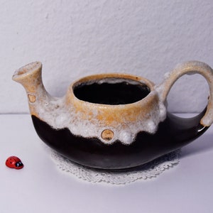 Könnte beinhalten: Eine braune und weiße Teekanne aus Keramik mit einer einzigartigen Form und einer strukturierten Glasur. Die Teekanne hat einen Ausguss auf der einen Seite und einen Griff auf der anderen.