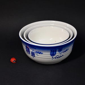 Könnte beinhalten: Ein Satz aus drei weißen Keramikschalen mit blauen Blumenmustern. Die Schalen sind ineinander verschachtelt, wobei die kleinste Schale oben liegt.